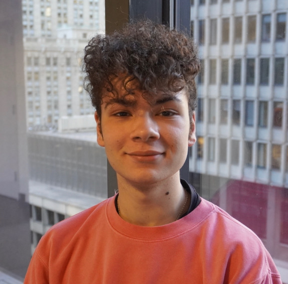 Headshot Thanasi Linda standing in a hallway with arms crossed, smiling.